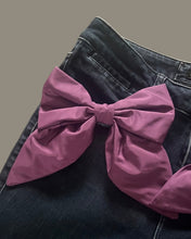 Load image into Gallery viewer, Plum silk statement bow brooch pinned to the hip of dark denim jeans.