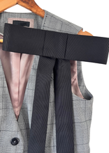 Load image into Gallery viewer, A close-up of a gray plaid blazer vest on a wooden hanger, featuring a wide black silk bow brooch pinned on the chest and long black tails hanging down. 
